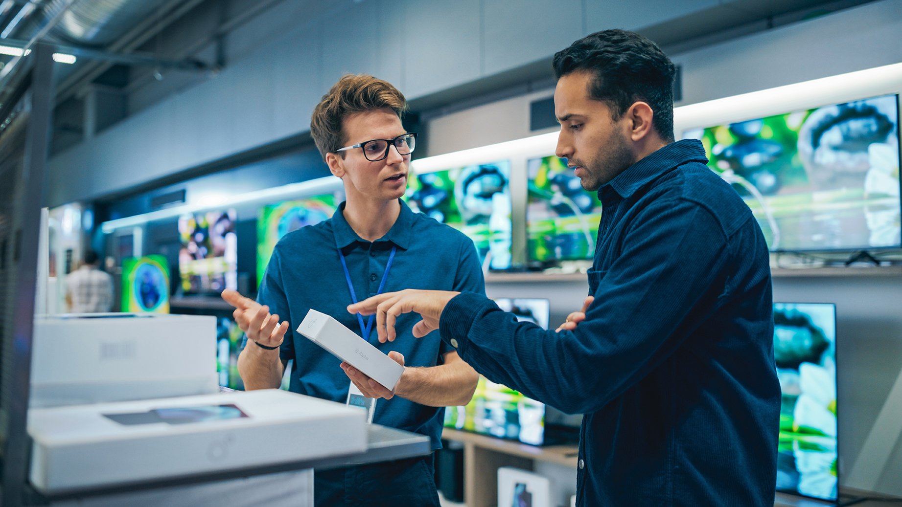 Young Multiethnic Customer Advising with Retail Home Electronics Store Salesperson. Stylish Man is Interested in Buying a Smartphone. Client Shopping for a New Cellphone in a Modern Shop
